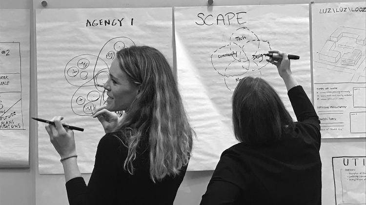 Black and white image of two individuals writing and drawing on wall hung note pads