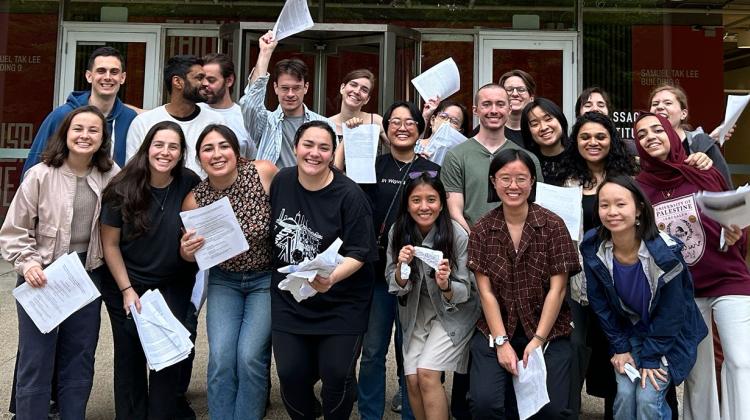 Group photo of students with copies of their theses in front of DUSP's building at MIT