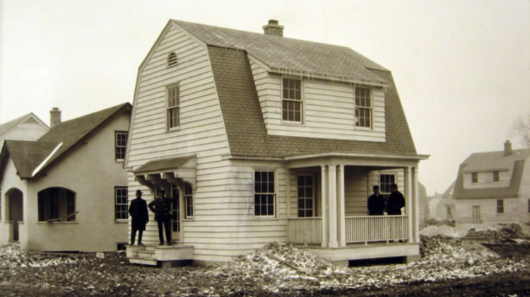 Sepia-toned photograph of a group of men standing in front of a newly-built house.